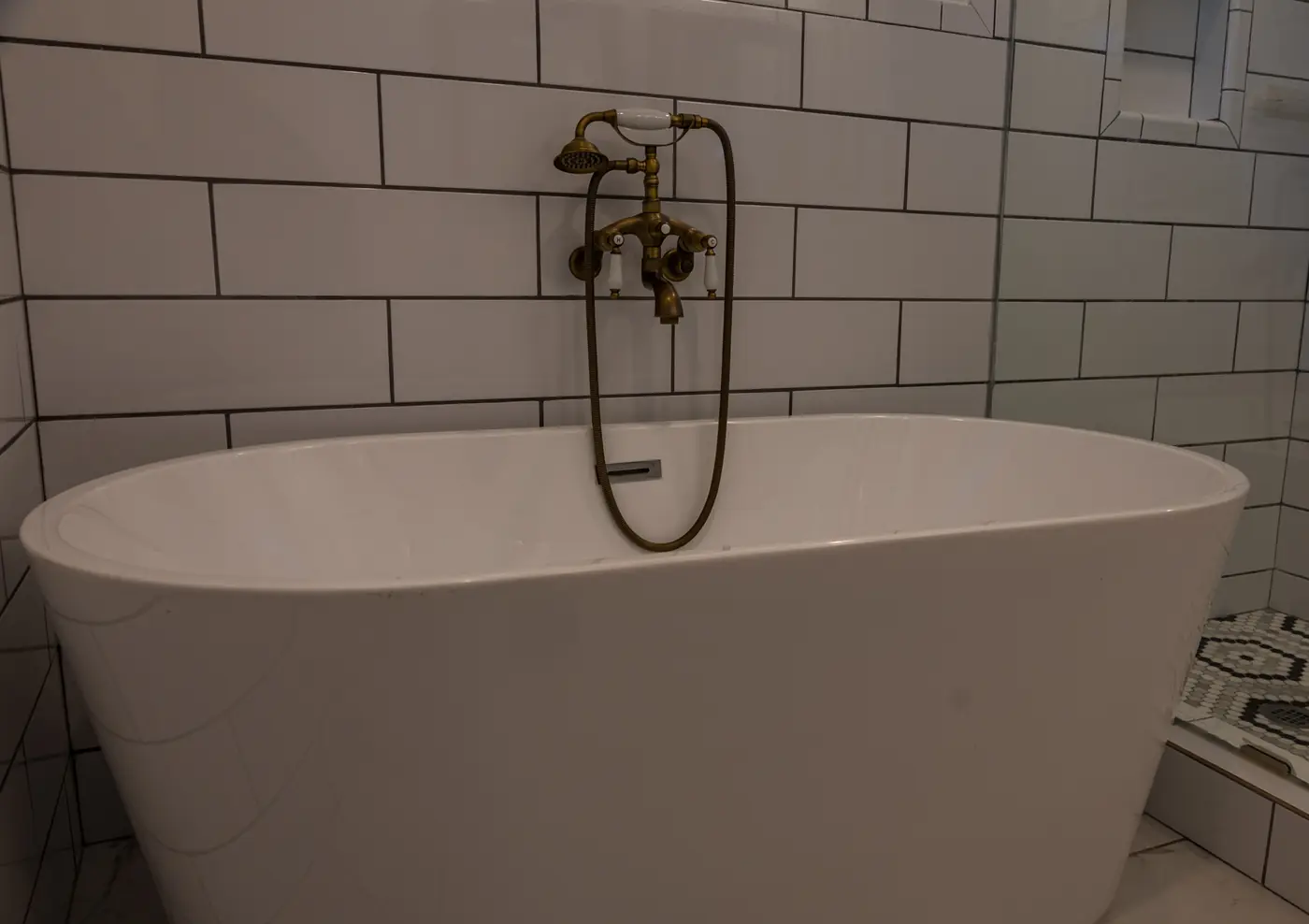 Freestanding soaking tub with a brass telephone-style tub filler and subway tile in Metairie, LA
